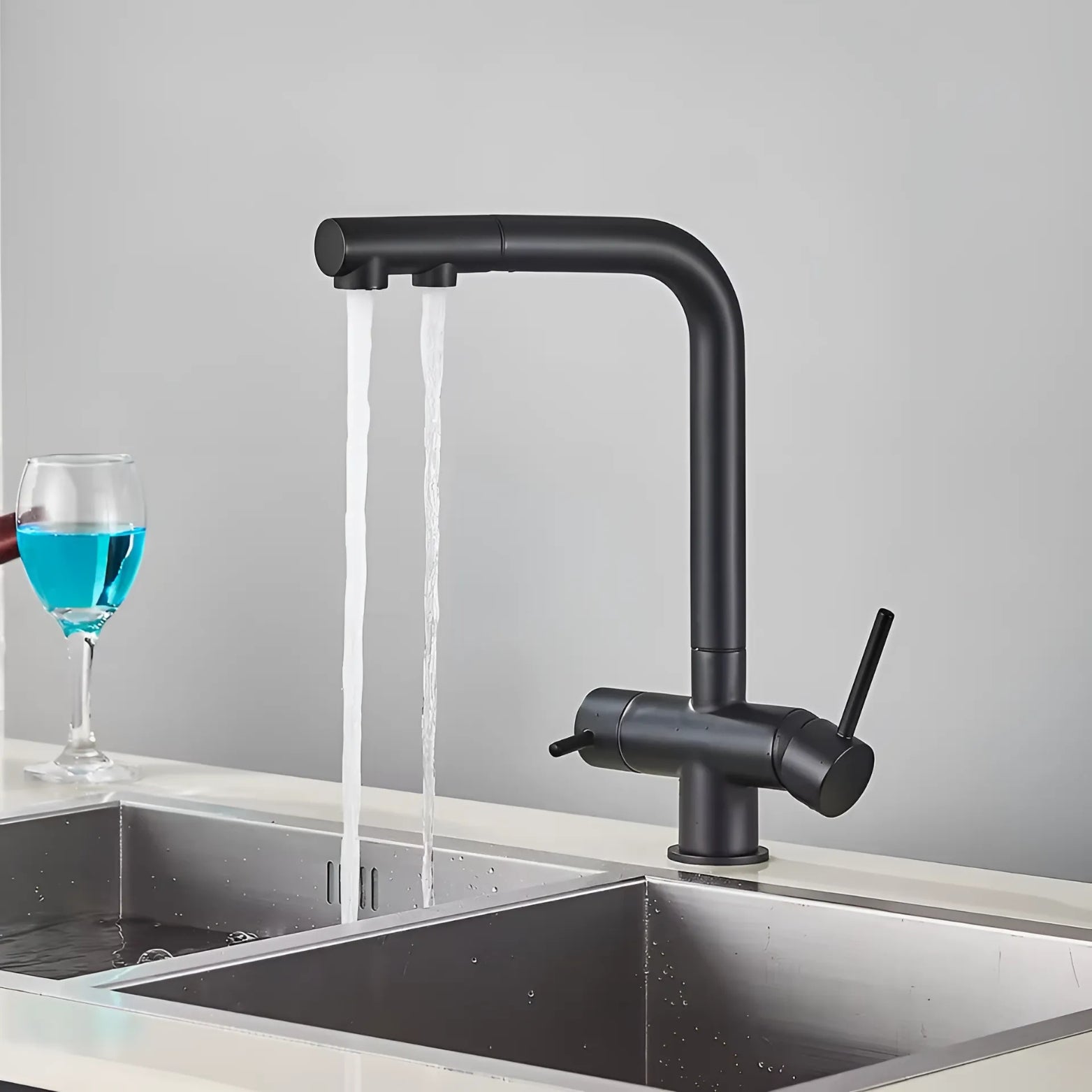 3-Way Pull-Out Black kitchen faucet with water flowing into a sink, with a glass of blue liquid on a gray background