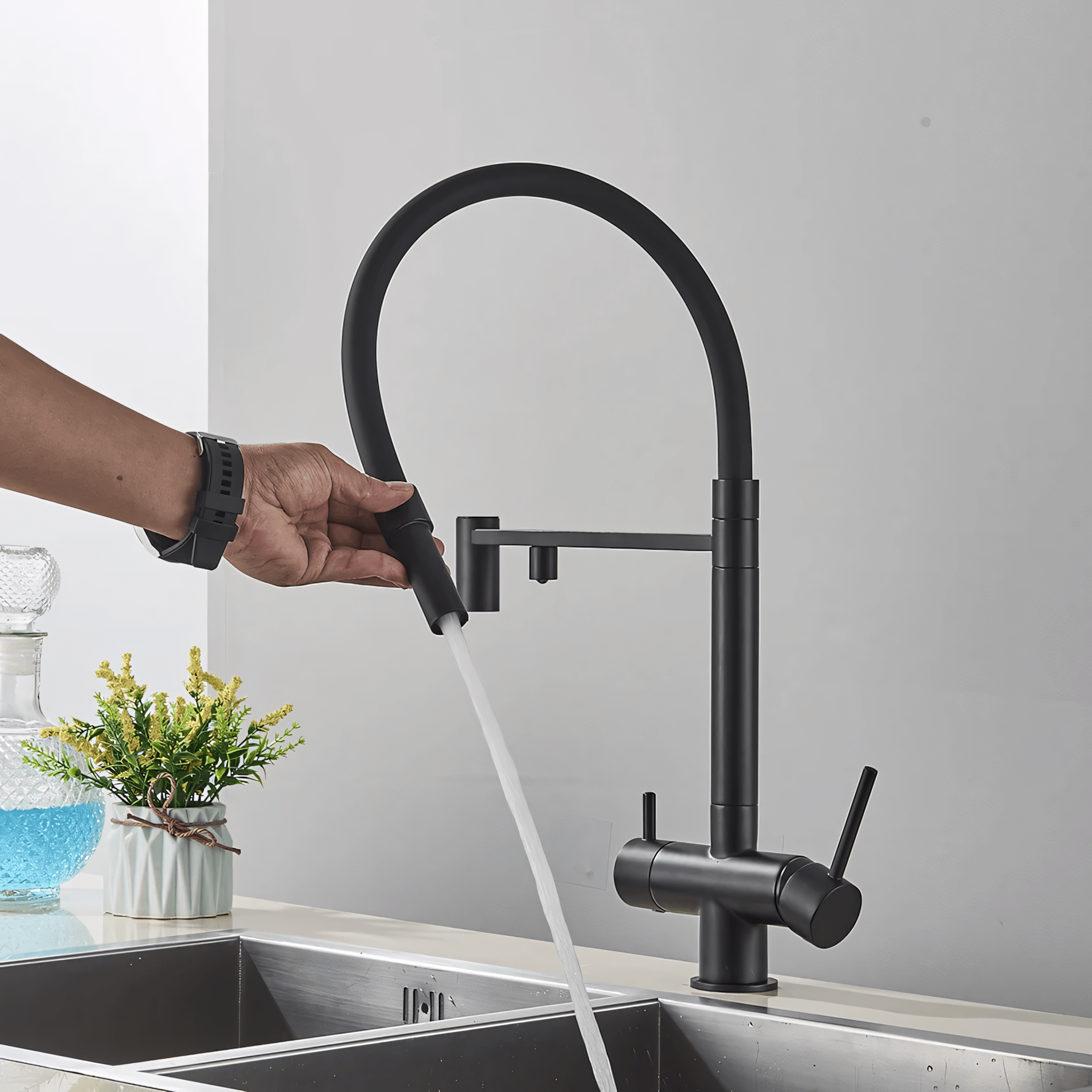 Black kitchen faucet being turned on with water flowing, set against a neutral background.