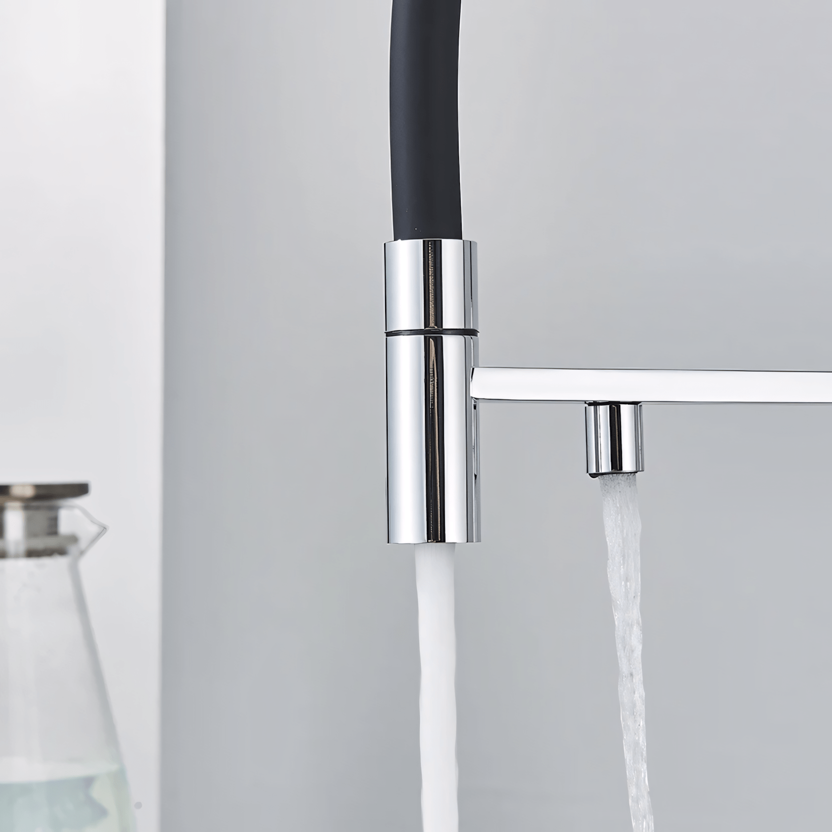 Chrome kitchen faucet with running water on a light gray background